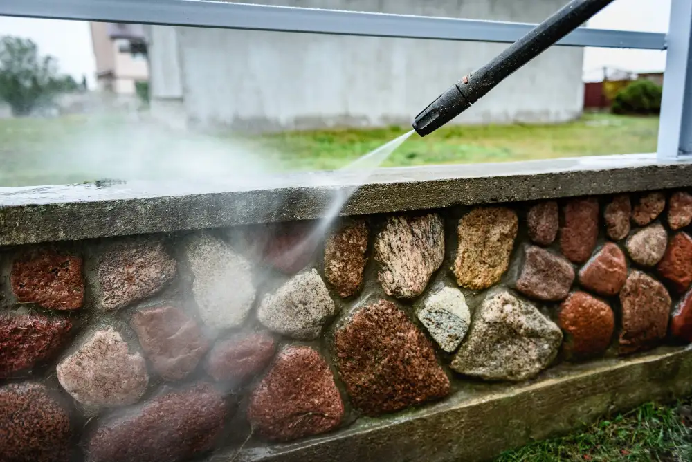 A gardener cleaning a wall using a pressure washer.